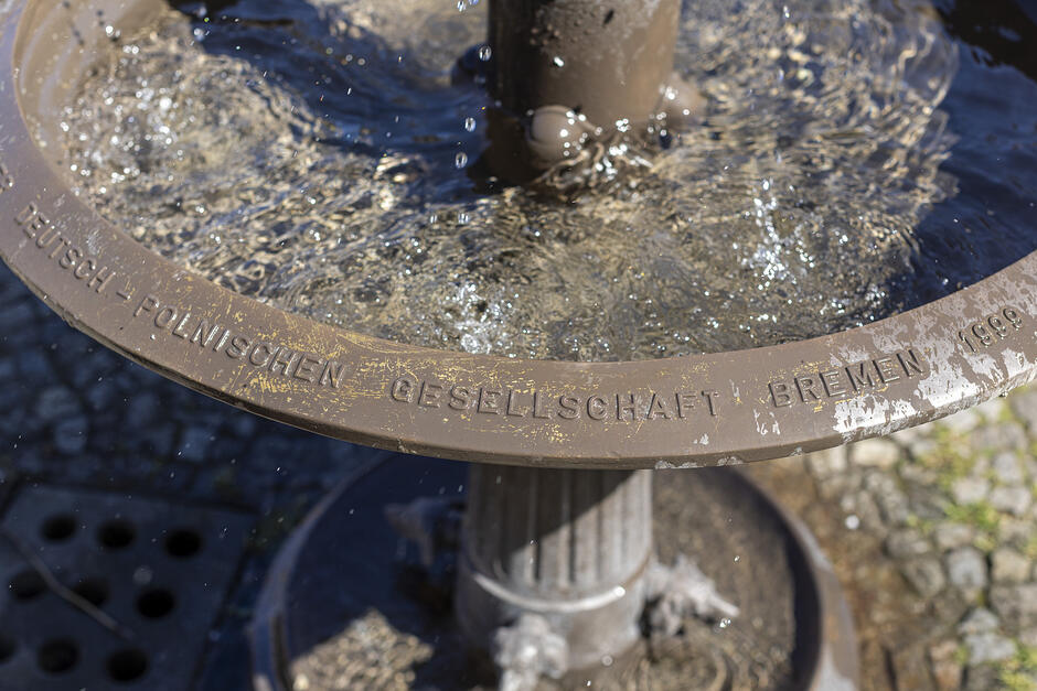 Fragment metalowej fontanny pokazujący część baseniku, do którego ciurka woda.