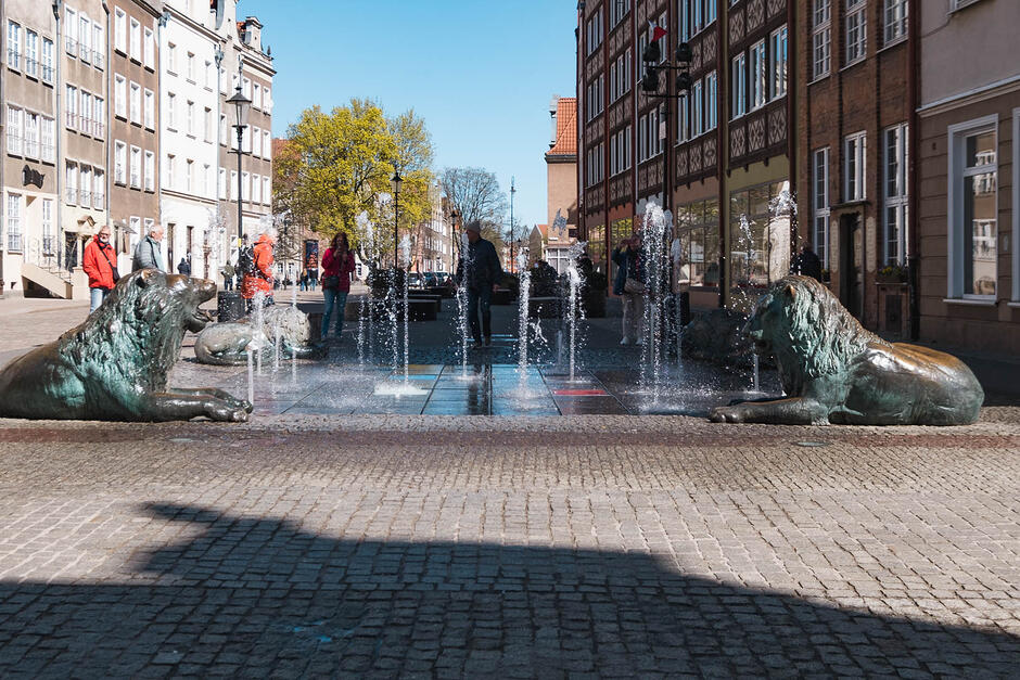 Fontanna z lwami na miejskim placu, a przy niej ludzie.