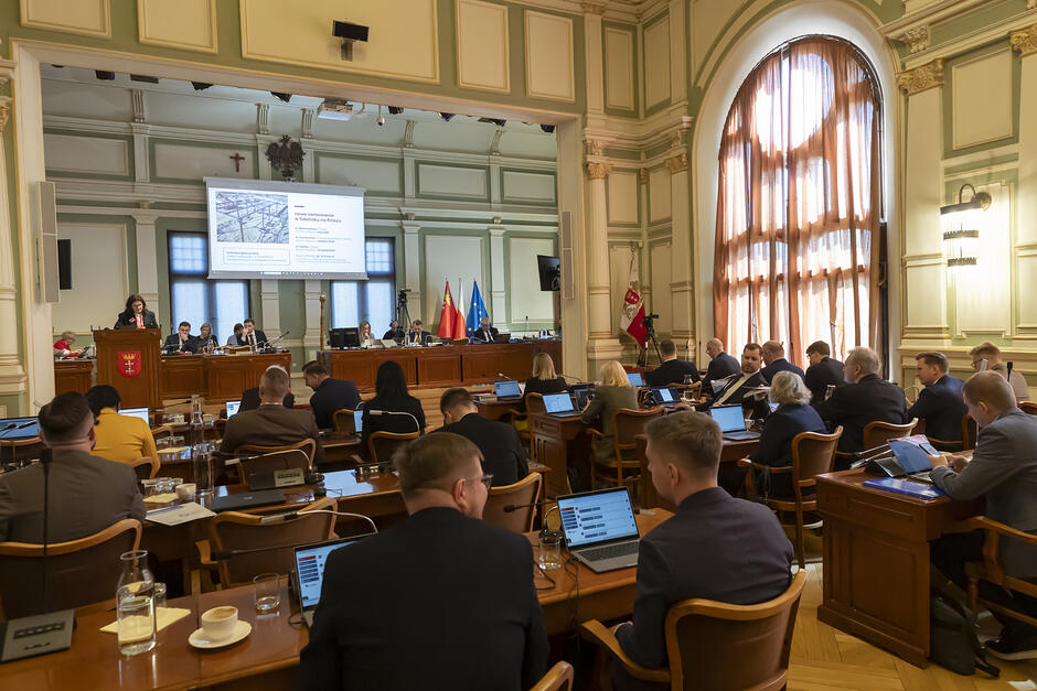 na zdjęciu zabytkowa, elegancka sala obrad rady miasta, widać dwóch mężczyzn siedzących tyłem do fotografującego