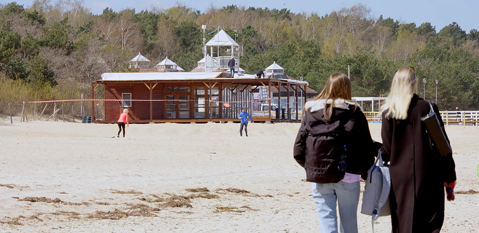 Plaża. W tle beach bar, który dopiero powstaje. Z prawej strony dwie spacerujące brzegiem morza kobiety.