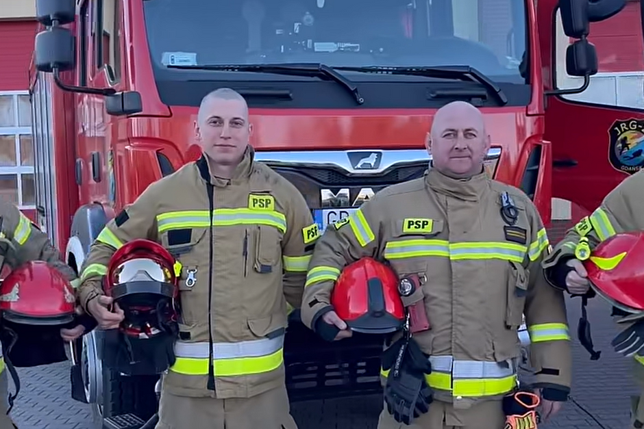 Łysi strażacy na tle wozu strażackiego