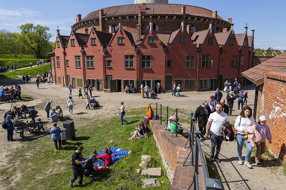 Stara ceglana twierdza, wokół której chodzą i siedzą ludzie podczas słonecznej pogody.
