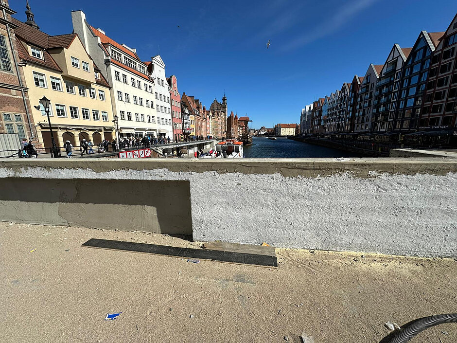 na zdjęciu zaszpachlowany, remontowany murek, w tle kilka kamienic po lewej stronie