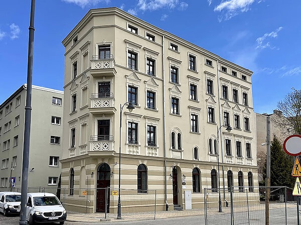Widok od frontu na wyremontowaną kamienicę przy ul. Dolnej 10A. Przed budynkiem stoją dwa białe samochody osobowe. 