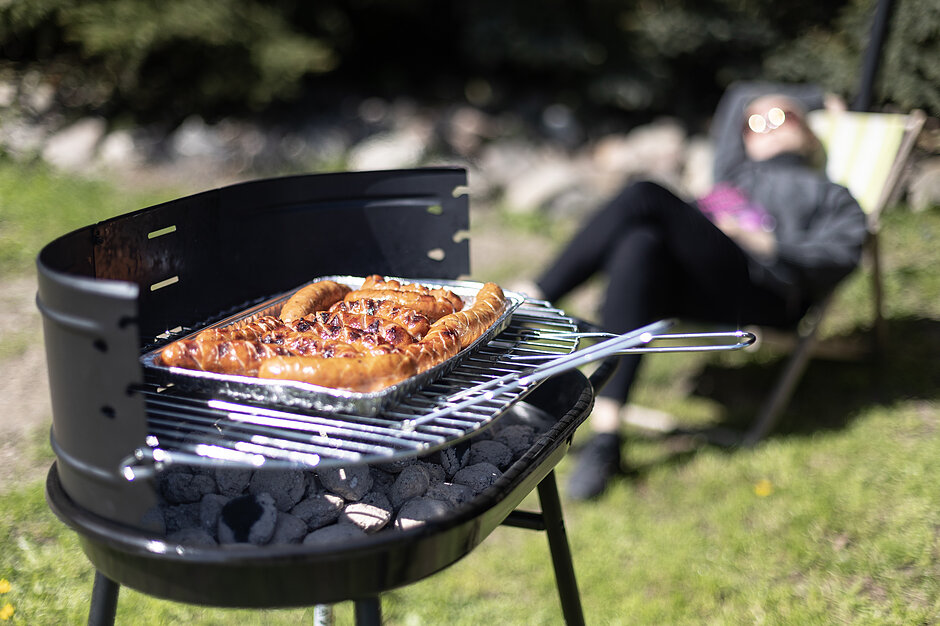 Grill na pierwszym planie. W tle widzimy odpoczywającą osobę na leżaku.