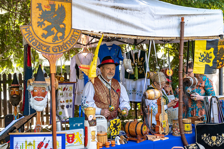 Mężczyzna w stroju regionalnym przy stoisku z kolorowymi ozdobami 