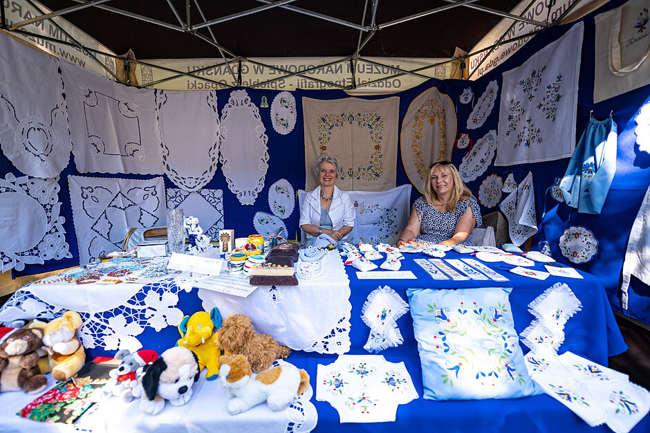 Haficiarki siedzą przy stoisku z wyhaftowanym rękodziełem