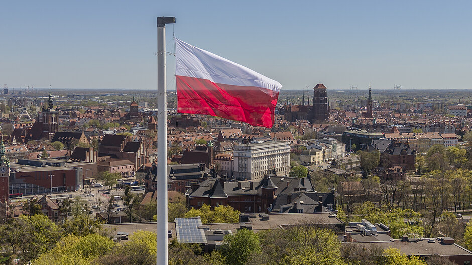 biało czerwona flaga powiewa nad miastem, które widać w tle