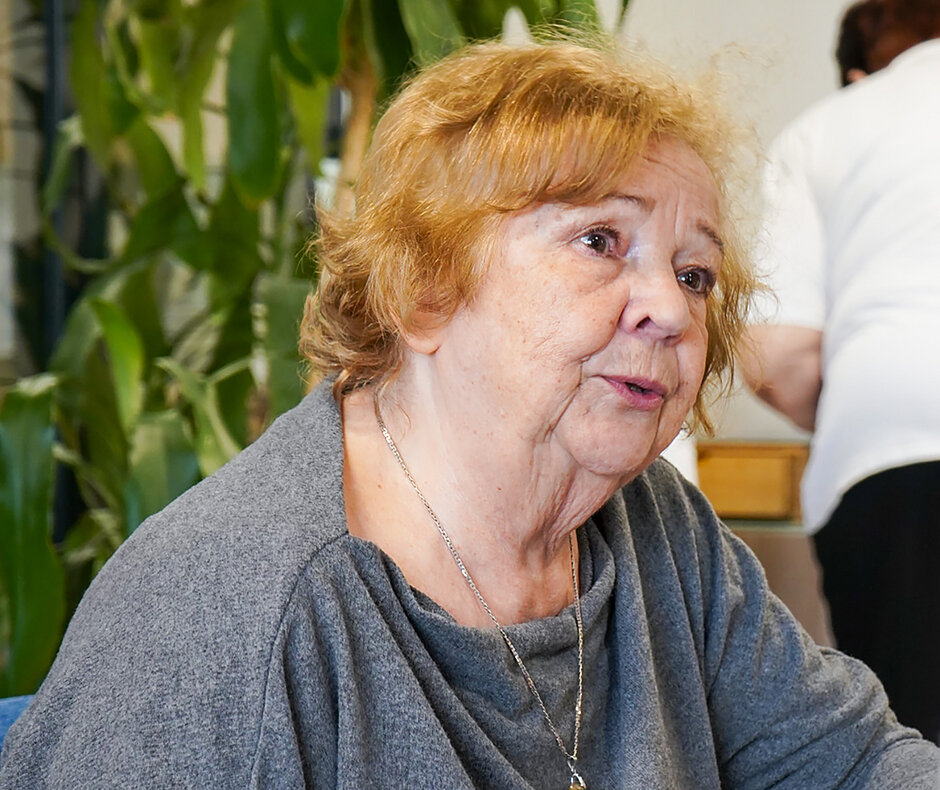 Kobieta, seniorka siedzi przy stoliku w kawiarni i z kimś rozmawia. Rozmówcy nie widac w kadrze.