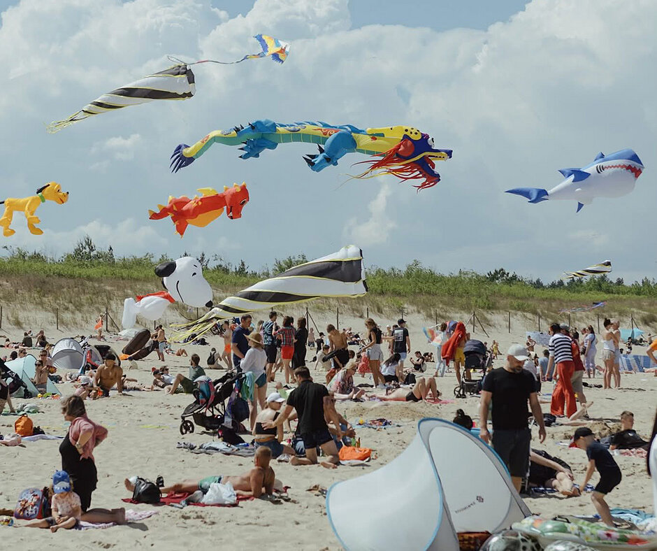 Wiele latawców lata nad plażą, na której jest tłum ludzi. 