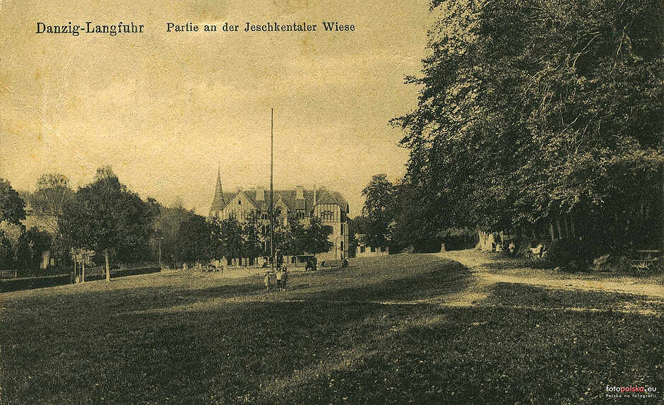 Archiwalna pocztówka w sepii przedstawia dawny widok na Łąkę Festynową w gdańskiej dzielnicy Wrzeszcz. Na otwartej, zielonej przestrzeni otoczonej drzewami widać w oddali zabytkową kamienicę z charakterystyczną wieżyczką, która stoi przy ulicy Jaśkowa Dolina.