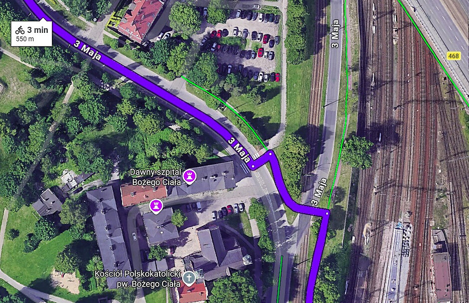 Obraz przedstawia widok satelitarny na fragment ulicy 3 Maja w Gdańsku z nałożoną fioletową trasą rowerową o długości 550 metrów. Na mapie widoczne są również tory kolejowe, parking samochodowy oraz obiekty historyczne, w tym dawny szpital Bożego Ciała.