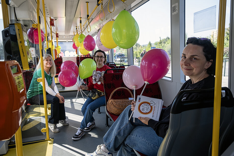 Trzy kobiety uśmiechają się we wnętrzu tramwaju z balonami.