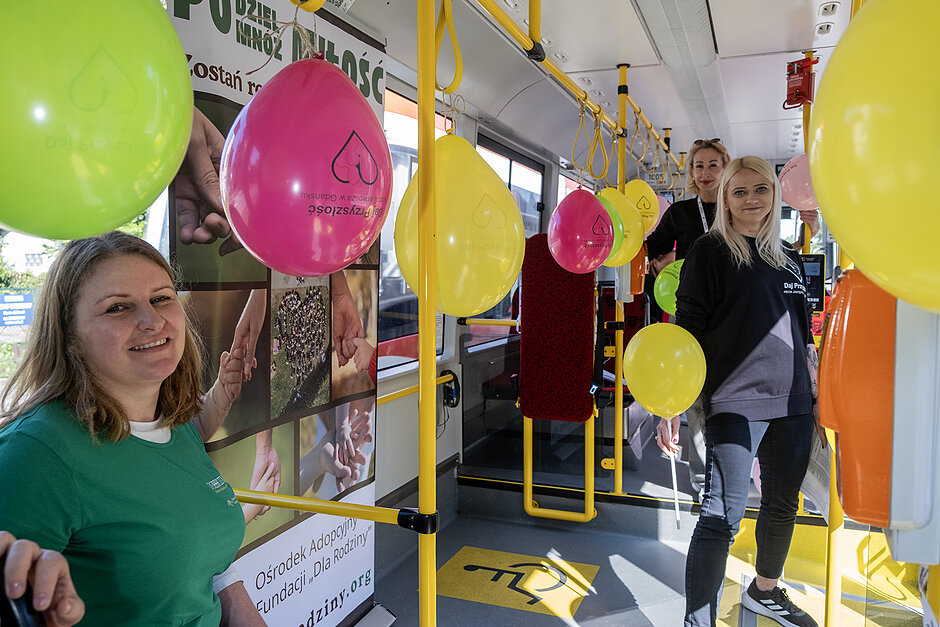 Trzy kobiety śmieją się we wnętrzu tramwaju z balonami. 