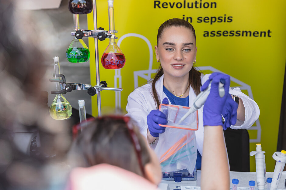 Kobieta w białym fartuchu robi eksperyment chemiczny, przed nią dzieci.