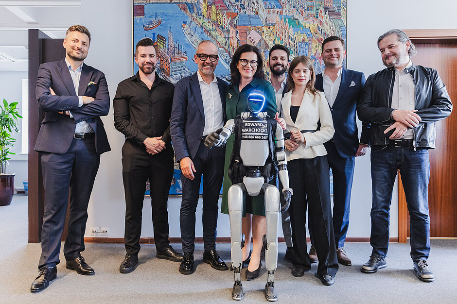Grupa ludzi stoi z robotem humanoidalnym