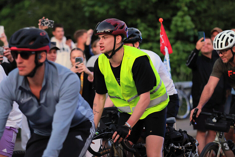 Rowerzysta w seledynowej kamizelce, jedzie pośród grupy rowerzystów