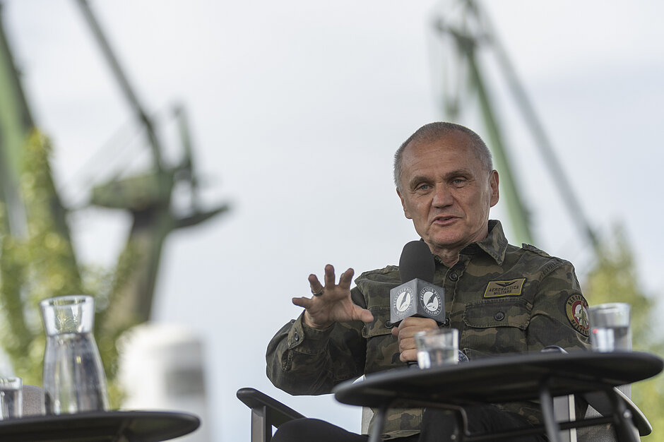na zdjęciu mężczyzna w średnim wieku, mówi do mikrofonu