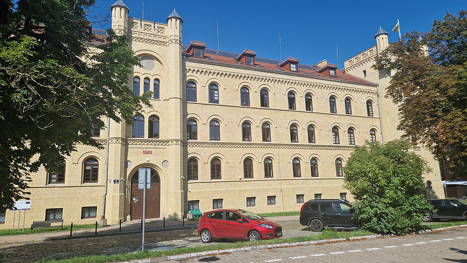 Parking przed dużym budynkiem z żółtej cegły