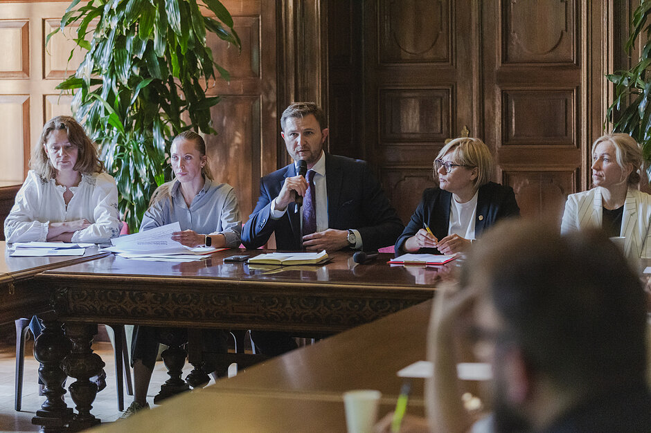 na zdjęciu wiceprezydent Piotr grzelak siedzi za stołem, mówi do mikrofonu, obok niego siedzą trzy urzędniczki, po obu jego stronach