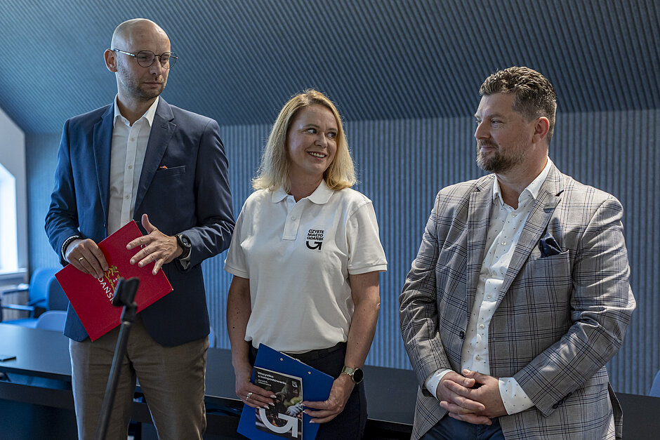 Trzy osoby stoją podczas briefingu medialnego