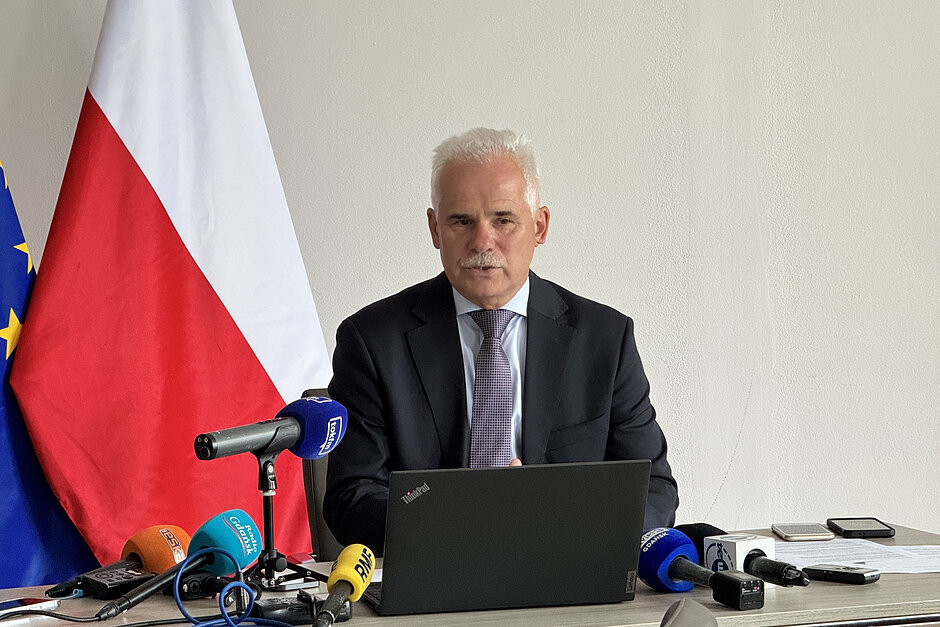 Mężczyzna w średnim wieku, siedzi za biurkiem podczas konferencji