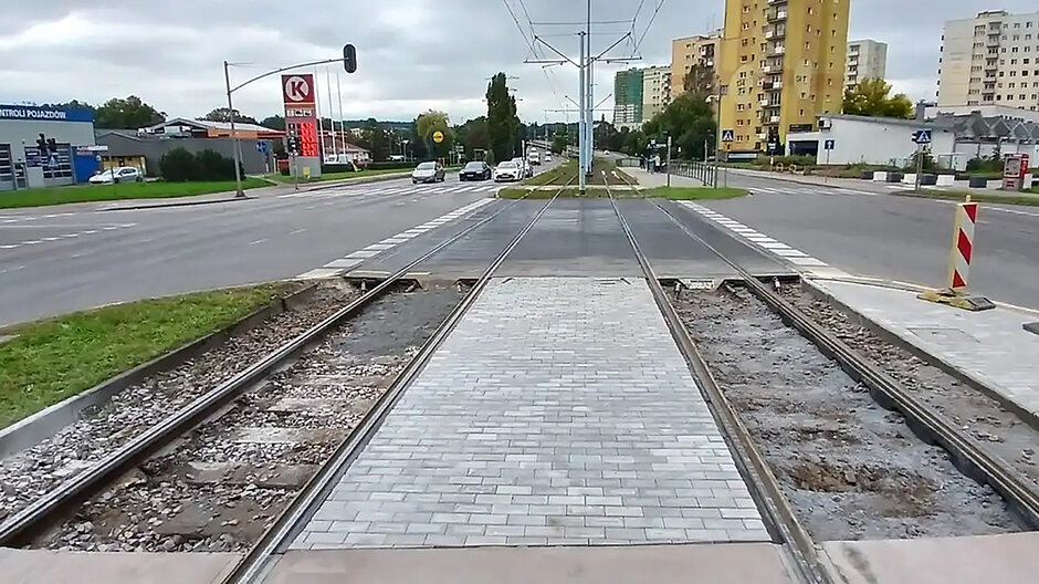 Skrzyżowanie torów tramwajowych i ulicy, w tle budynki mieszkalne.