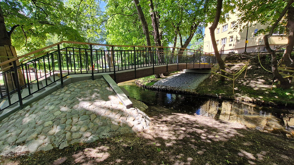 zdjęcie nowej kładki nad potokiem, widać w tle trawniki i drzewa