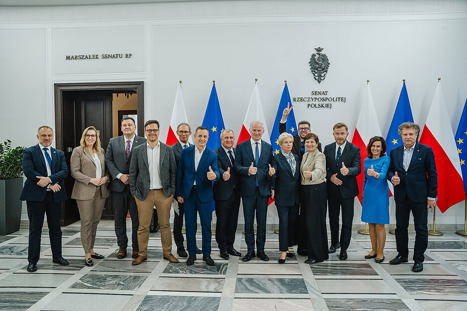 Grupa kilkunastu rozradowanych osób pozuje do wspólnego zdjęcia w korytarzu gmachu Senatu