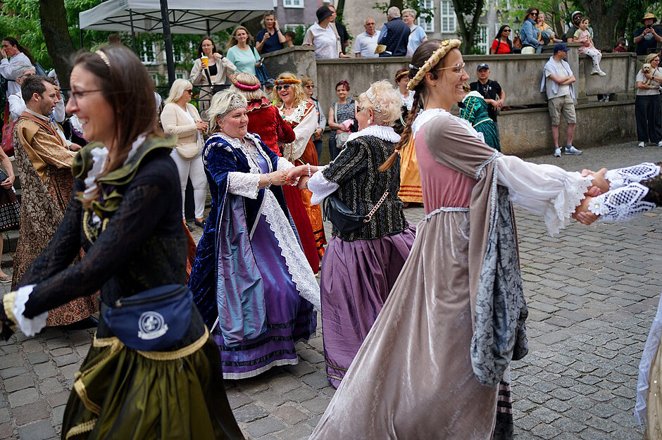 kobiety w historycznych sukniach tańczą na ulicy