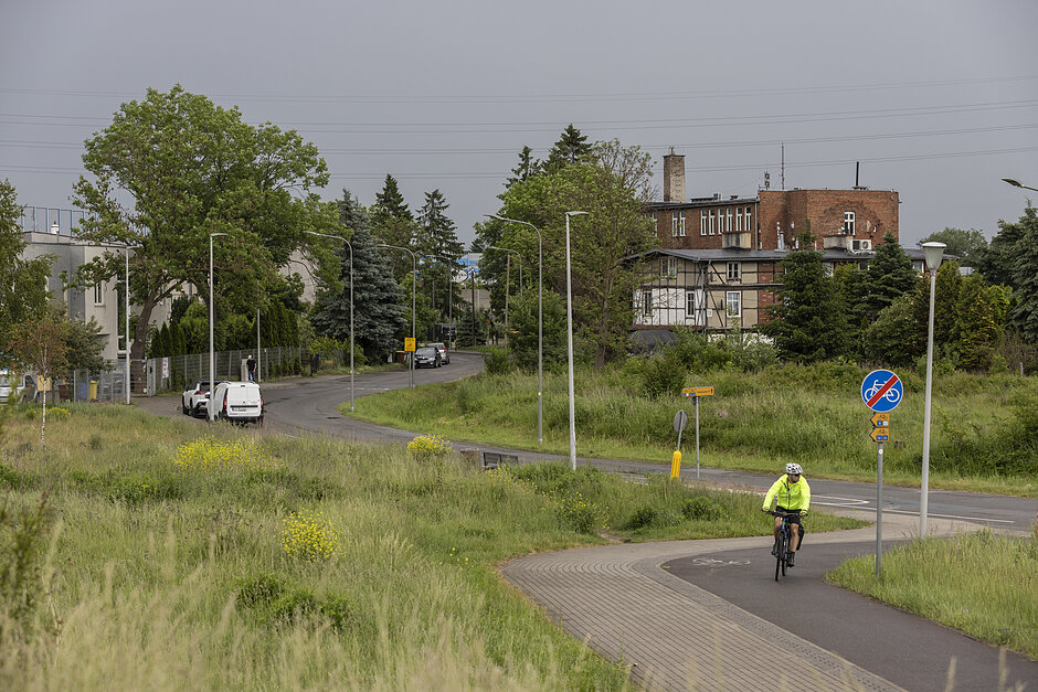 na zdjęciu rowerzysta jadący drogą rowerową, widać w tle ulicę i zabudowę niewysoką po prawej stronie