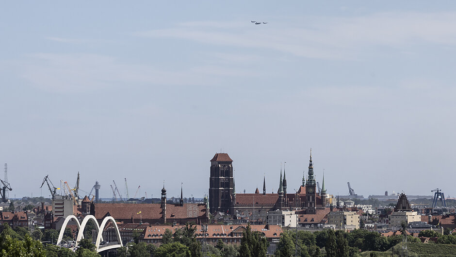 Małe punkciki samolotów w oddali na niebieskim niebie - poniżej panorama starego Gdańska