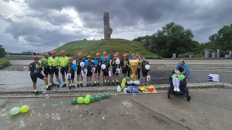 grupa rowerzystów pozuje pod pomnikiem