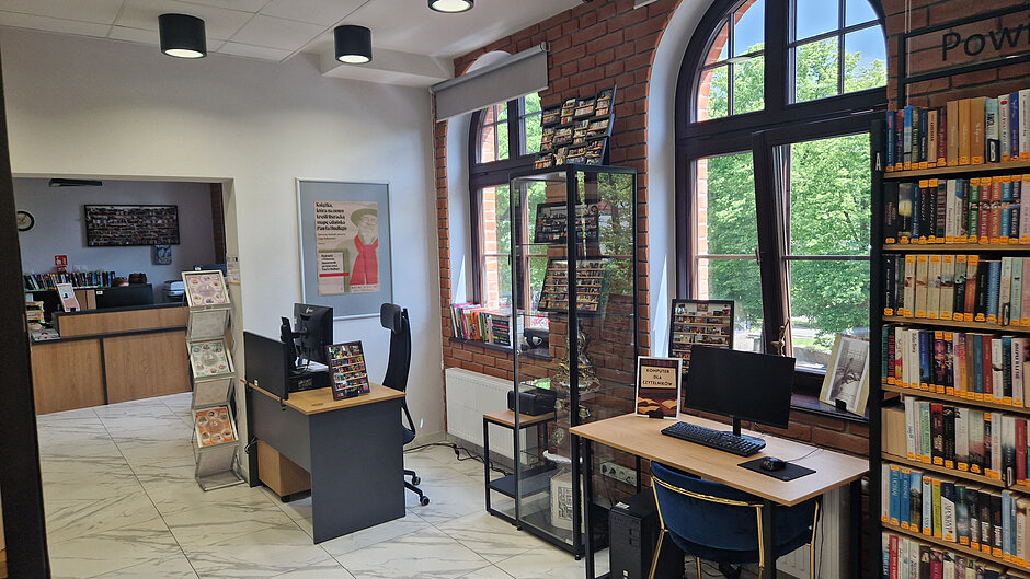 Wnętrze biblioteki z dużymi regałami i małymi w gablocie i na biurku