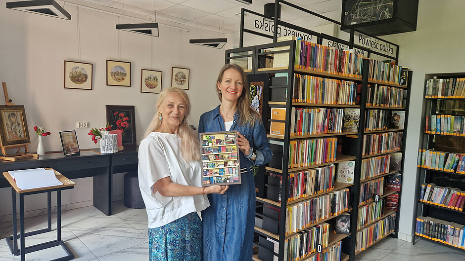 Dwie kobiety trzymające ramkę z miniaturową biblioteczką
