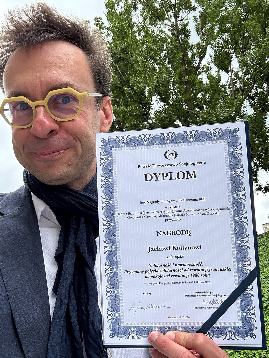 Uśmiechnięty szczupły mężczyzna w okularach prezentuje dyplom