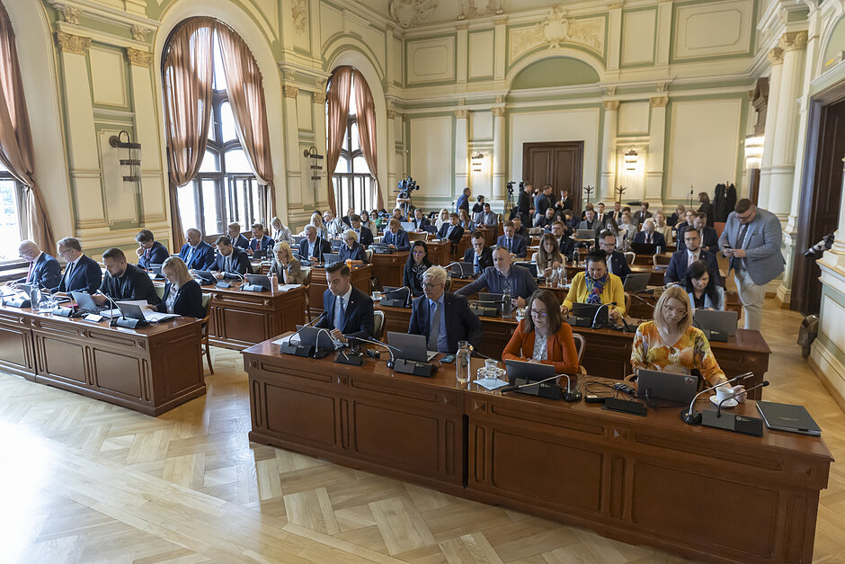 Widok sali obrad, w której za stołami siedzą radni