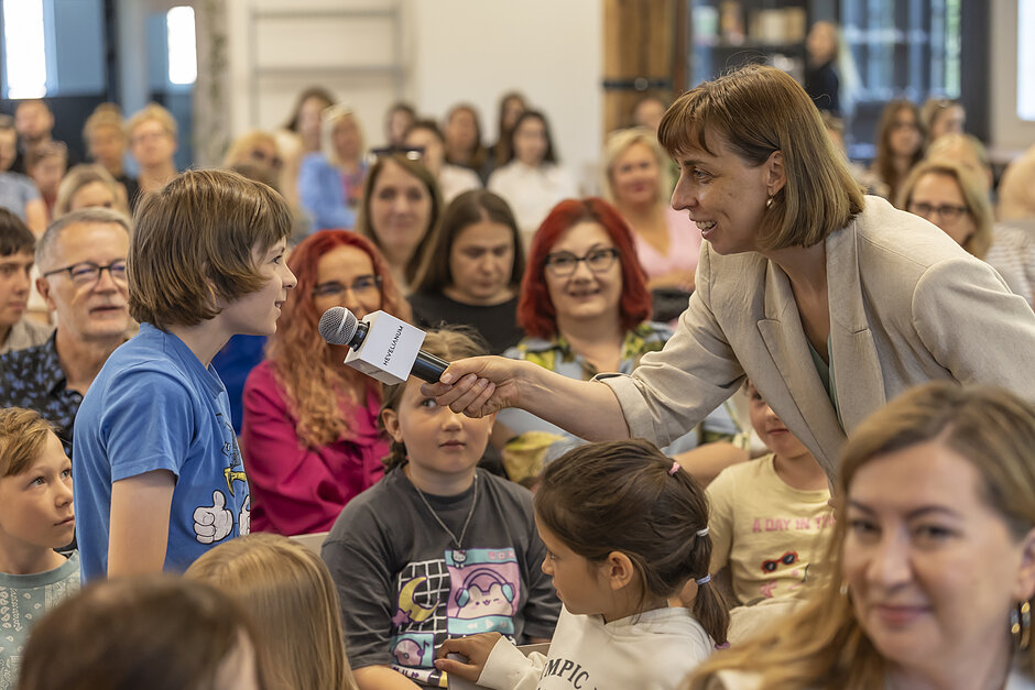 Kobieta podstawia mikrofon do wypowiedzi dziecku w sali konferencyjnej.