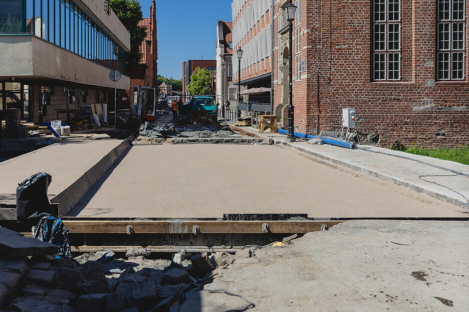 zbliżenie na remontowany most na który wylano właśnie świeży beton, w tle kilka budynków po obu stronach ulicy