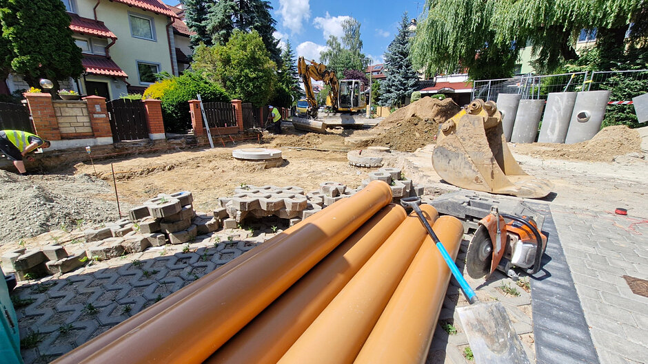 plac budowy, widać rozkopaną drogę z której zdjęto nawierzchnię, po prawej leżą rury