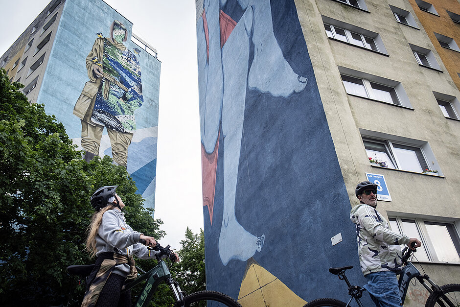 Kobieta i mężczyzna na rowerach oglądają murale na blokach.