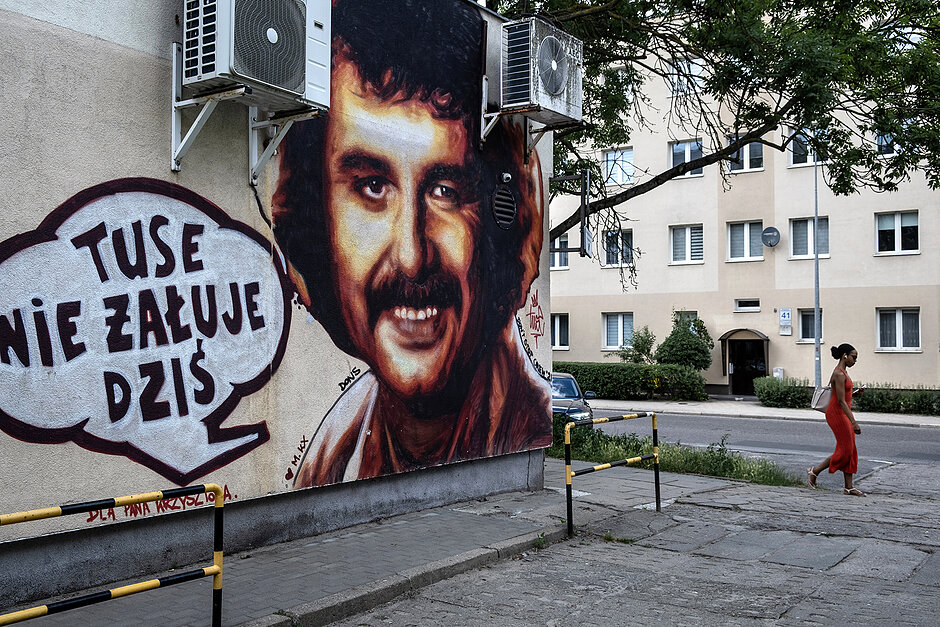 Mural z Krzysztofem Krawczykiem, obok którego przechodzi chodnikiem kobieta.