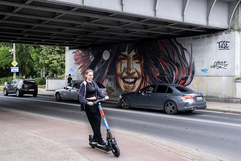 Mural z uśmiechniętą dziewczyną pod wiaduktem kolejowym.
