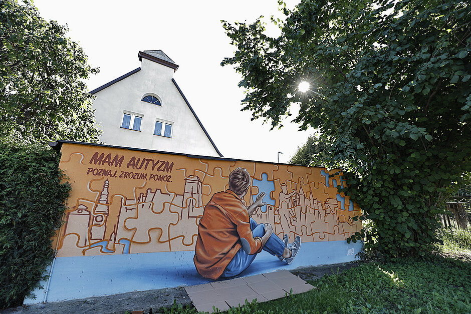 Mural na murze z chłopcem odwróconym tyłem do widza i przesłaniem o autyzmie.