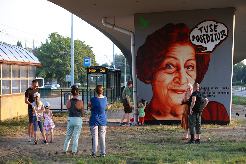 Mural z kobietą na słupie wiaduktu. Podziwia go kilka osób.