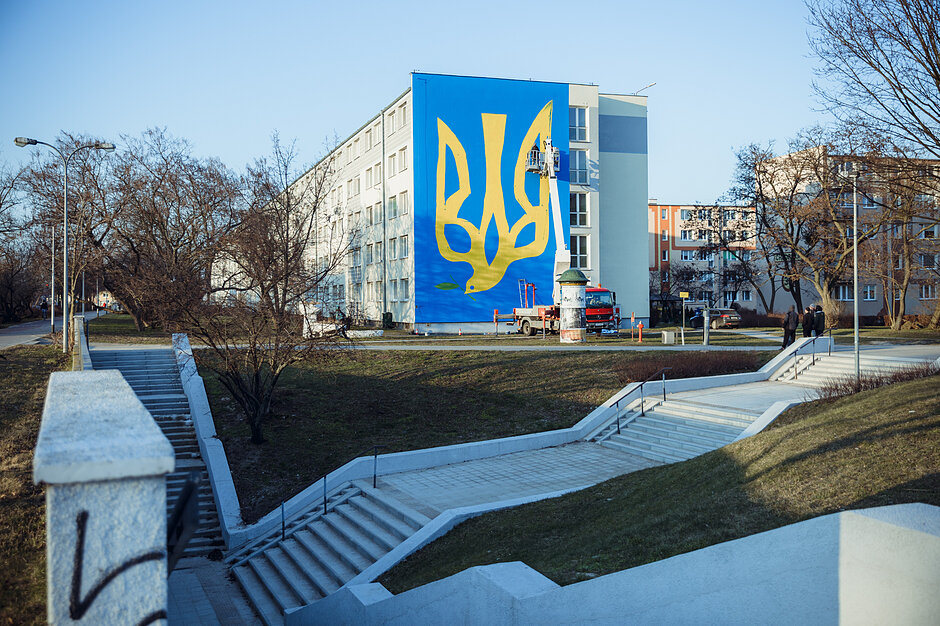 Mural solidarności z Ukrainą na bloku w trakcie malowania ze stojącego obok wysięgnika.