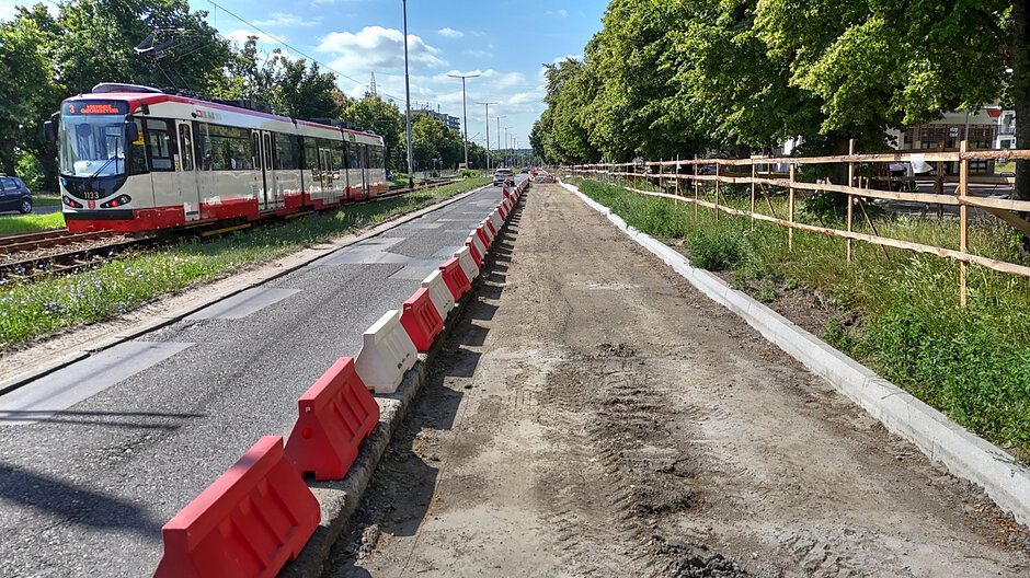 na zdjęciu po prawej rozkopana jezdnia, po lewej widać normalną jezdnię z nawierzchnią bitumiczną, w tle po lewej jedzie tramwaj