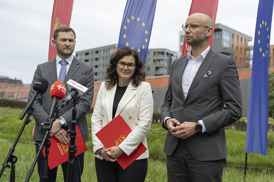 trzy wymienione osoby stoją przy mikrofonach