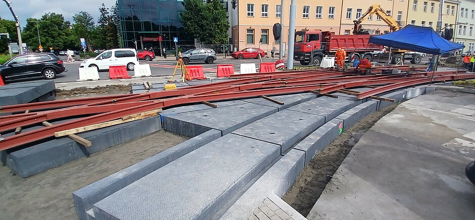 zbliżenie na nowe tory tramwajowe ułożone na betonowych podkładach, w tle budynki