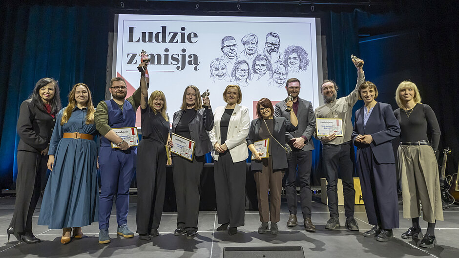 Grupa ludzi stoi razem na scenie na ciemnym tle